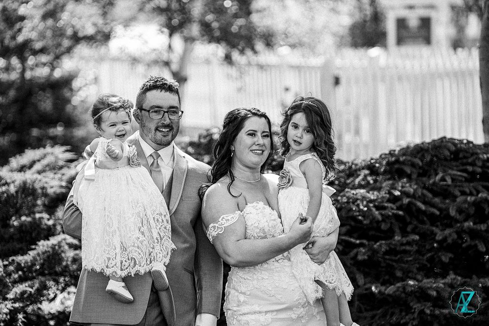 Black and white portrait of wedding party in a garden setting with white picket fence.