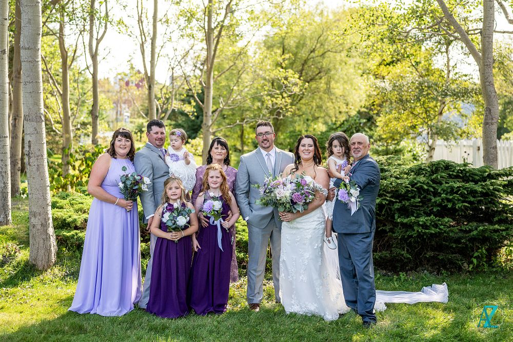 Wedding group photo in garden with bridesmaids in purple and lavender dresses holding bouquets.