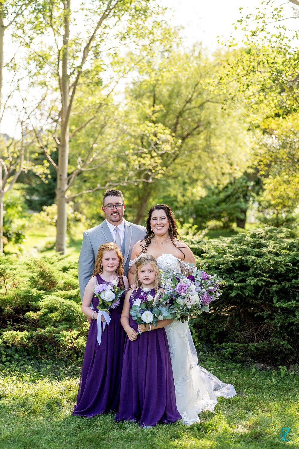 Garden wedding portrait with flowing white dress and purple flower girls' dresses.