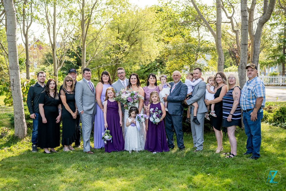 Extended wedding party gathering in garden setting wearing mix of formal and casual clothes.