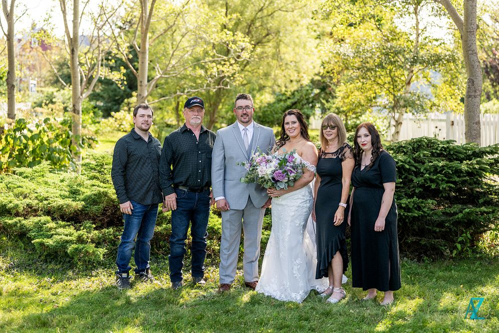 Group portrait of wedding party members standing together in a sunny garden landscape.