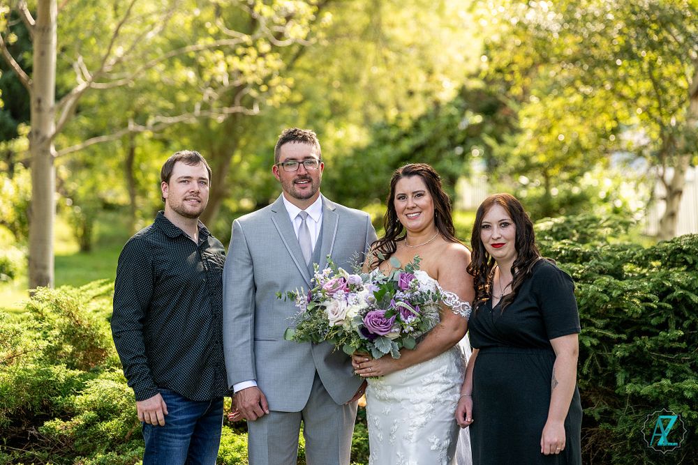 Wedding party poses outdoors in a garden setting with lush greenery and natural sunlight.