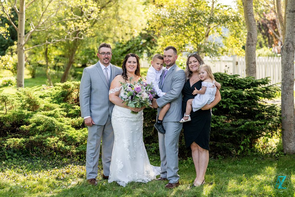 Wedding group photo with beautiful florals and greenery in an outdoor garden setting.