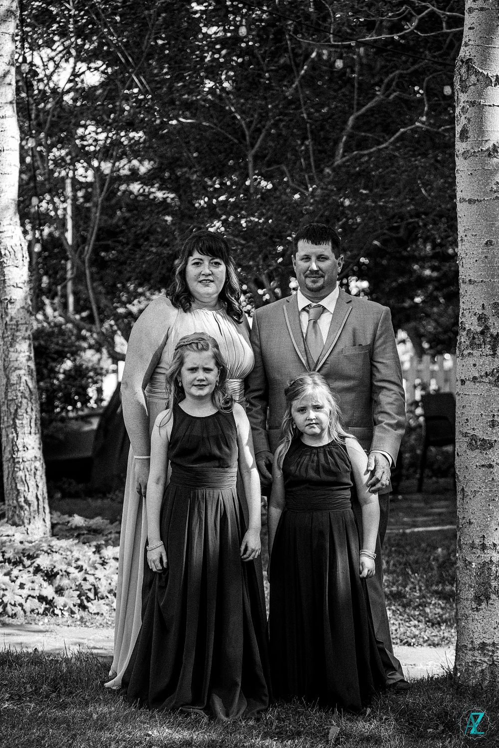 Black and white portrait of family in formal attire standing between birch trees.