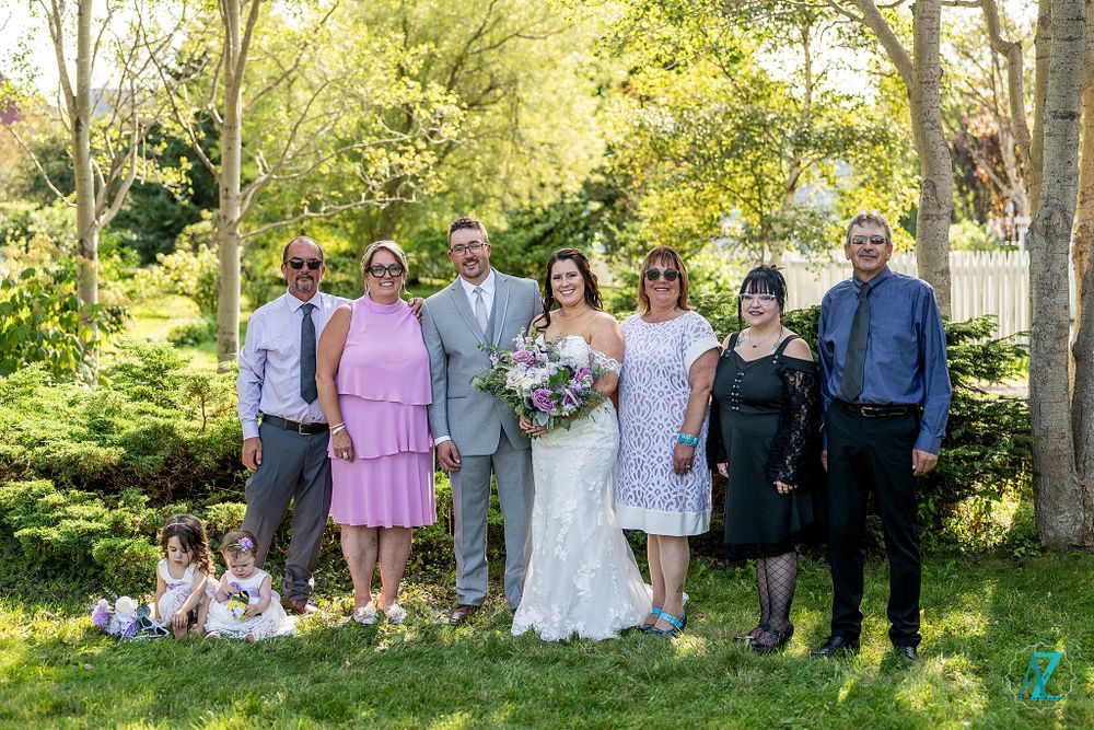 Large wedding party group photo with family members in outdoor garden setting.