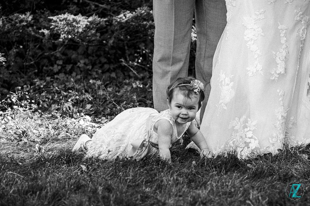 Black and white candid photo of small child crawling under wedding dress.