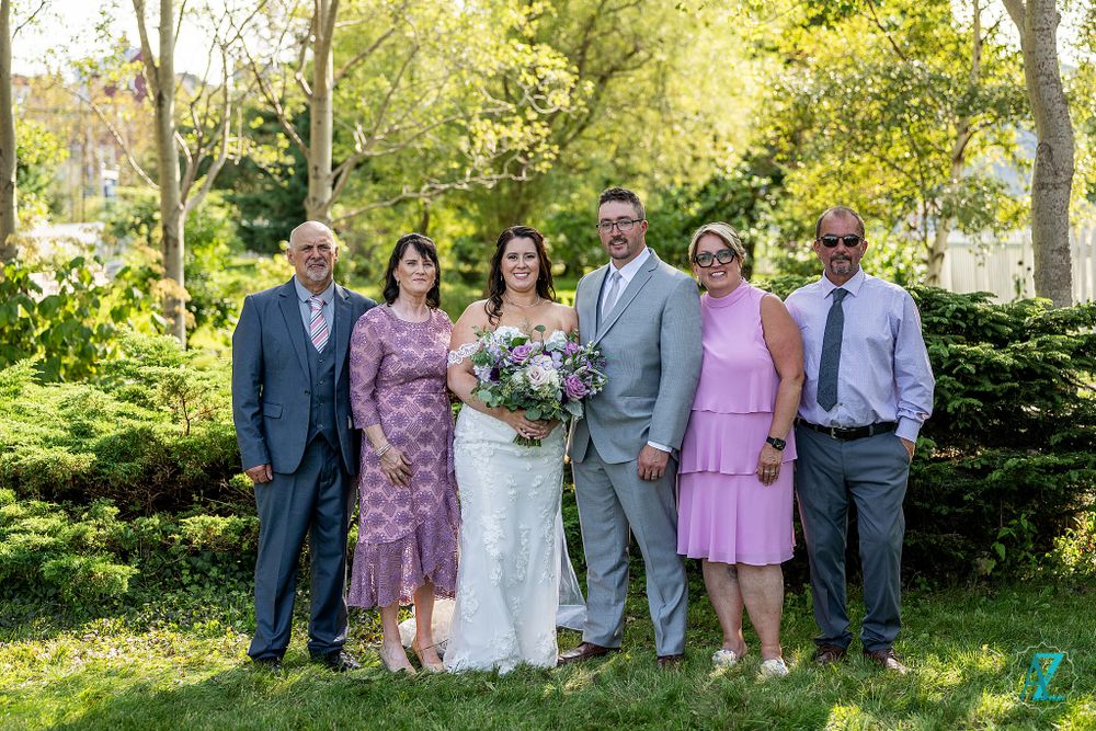 Wedding party poses together in garden setting with pink and gray color scheme.