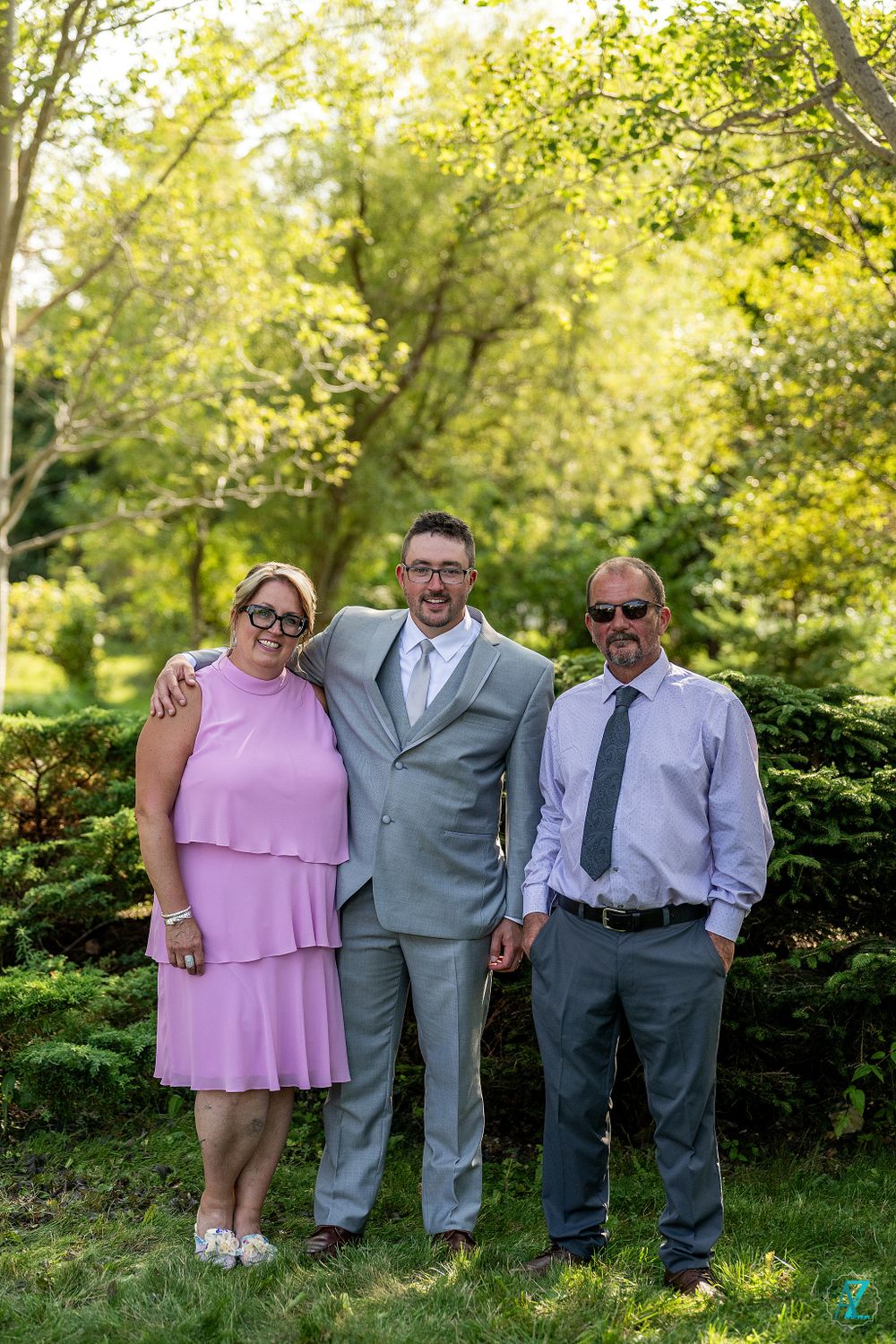 Three people pose together outdoors, with person in gray suit in center.