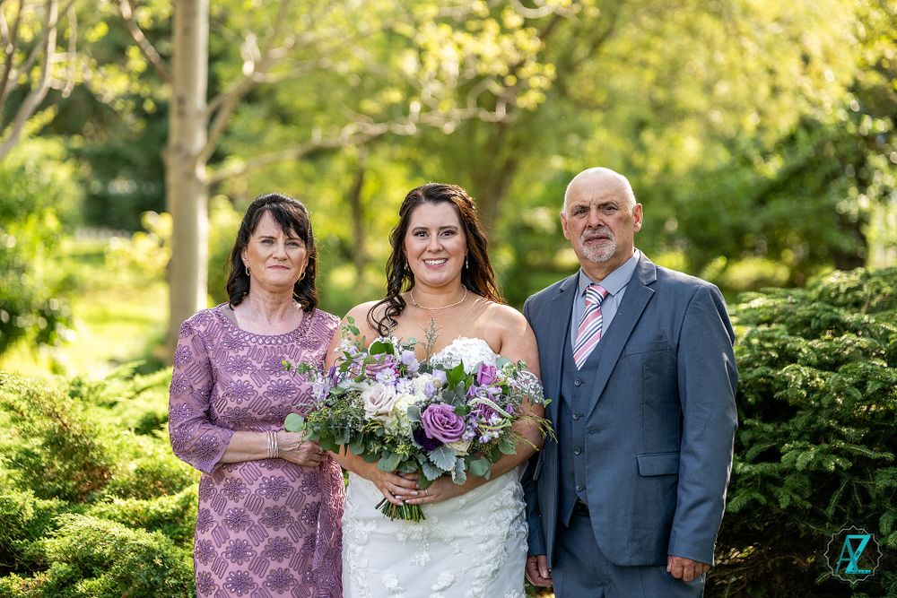 Wedding portrait with bride holding purple bouquet flanked by couple in garden setting.
