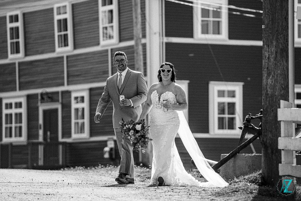 Black and white photo of wedding couple walking with dog on gravel path by house.