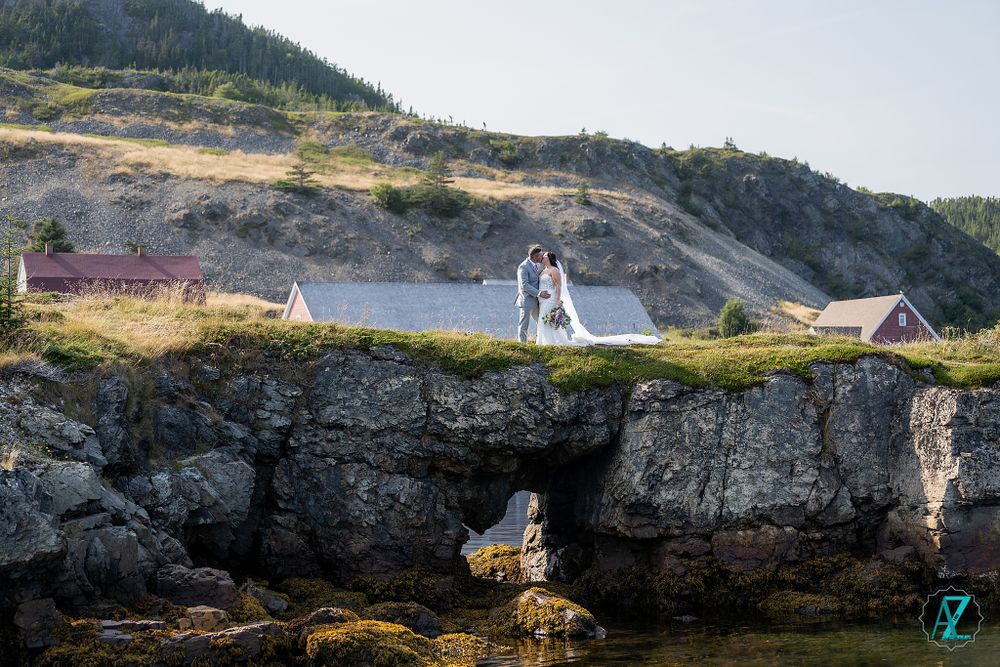 Coastal wedding portrait with couple standing on rocky cliffs above ocean inlet.