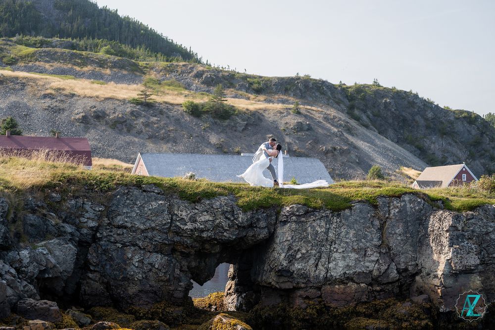 Scenic wedding photo of couple on rugged coastline with small houses and cliffs.