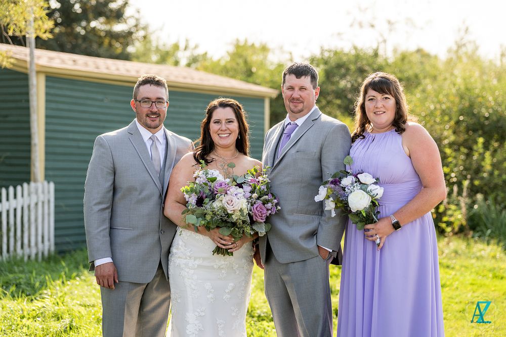 Wedding party in gray suits and lavender dresses poses together outdoors.