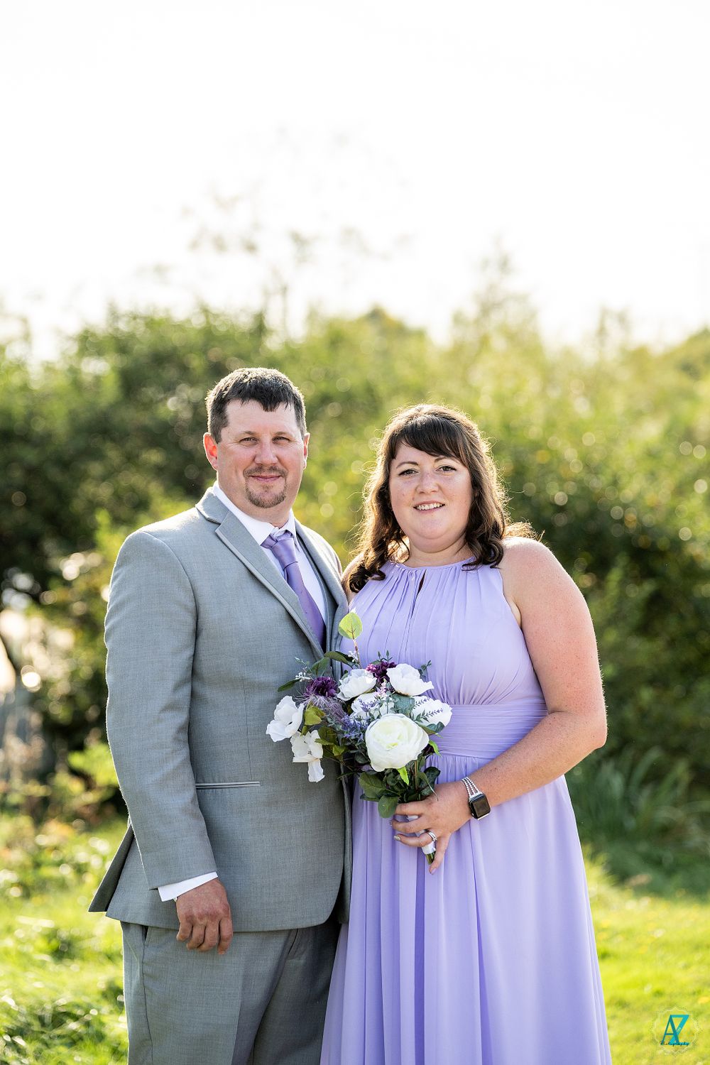 Wedding party members in gray suit and lavender dress pose with bouquet.