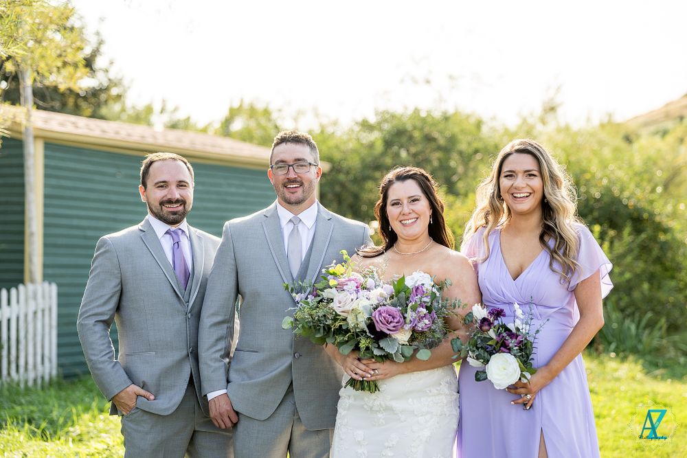 Wedding party poses outdoors with purple and white floral bouquets.
