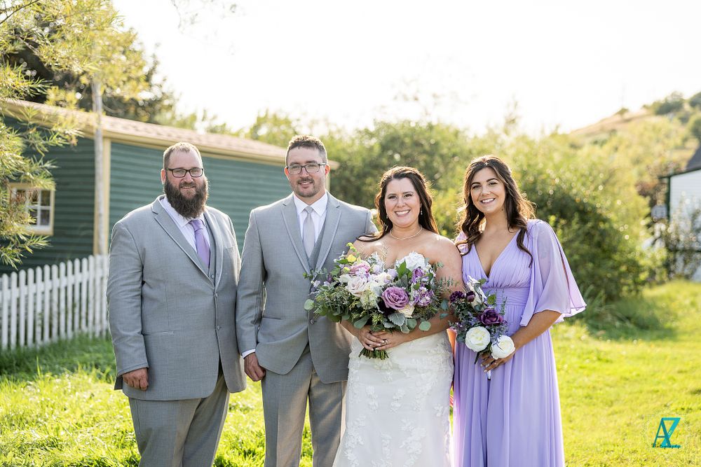 Wedding group in coordinated attire stands together on sunny lawn.