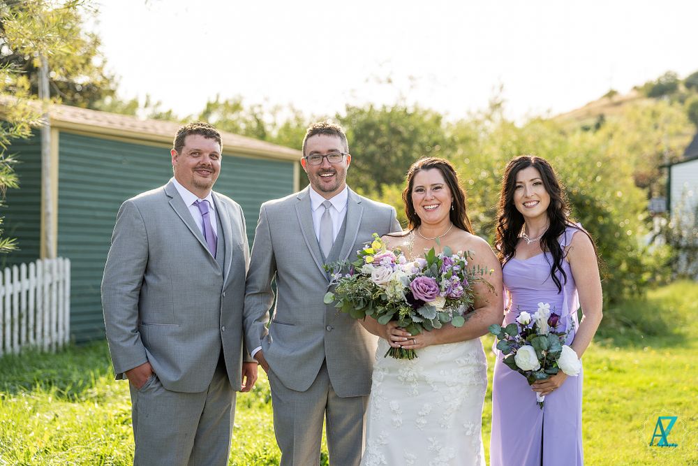 Wedding party members pose outdoors in gray suits and lavender dress with beautiful floral bouquets.
