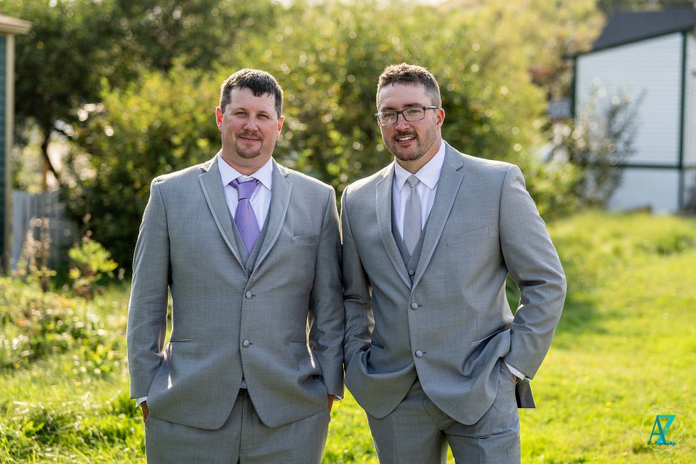 Two people in coordinated gray suits and purple ties stand together outdoors.