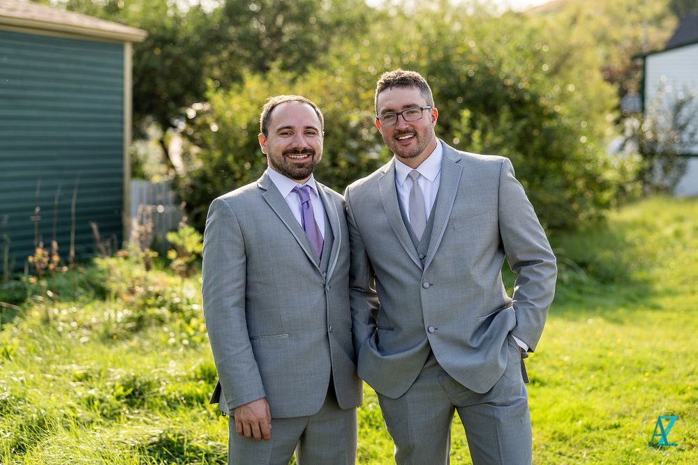Two people in gray suits with purple ties smile while standing on green lawn.
