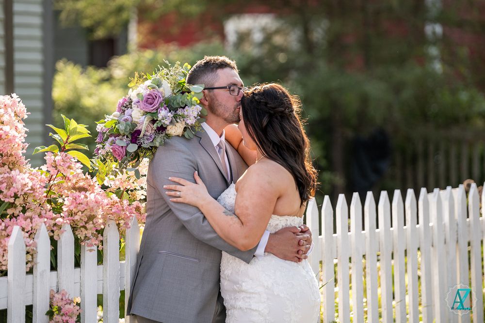 A romantic moment between newlyweds by a white picket fence with blooming flowers.