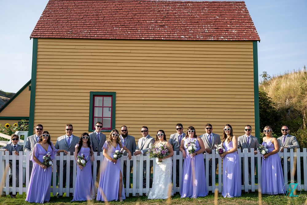 Wedding party in purple dresses and grey suits poses in front of a historic yellow building.