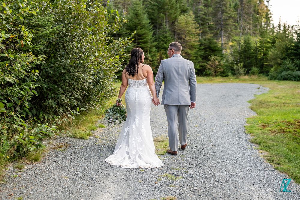 Wedding couple walks down a gravel path surrounded by lush forest scenery.