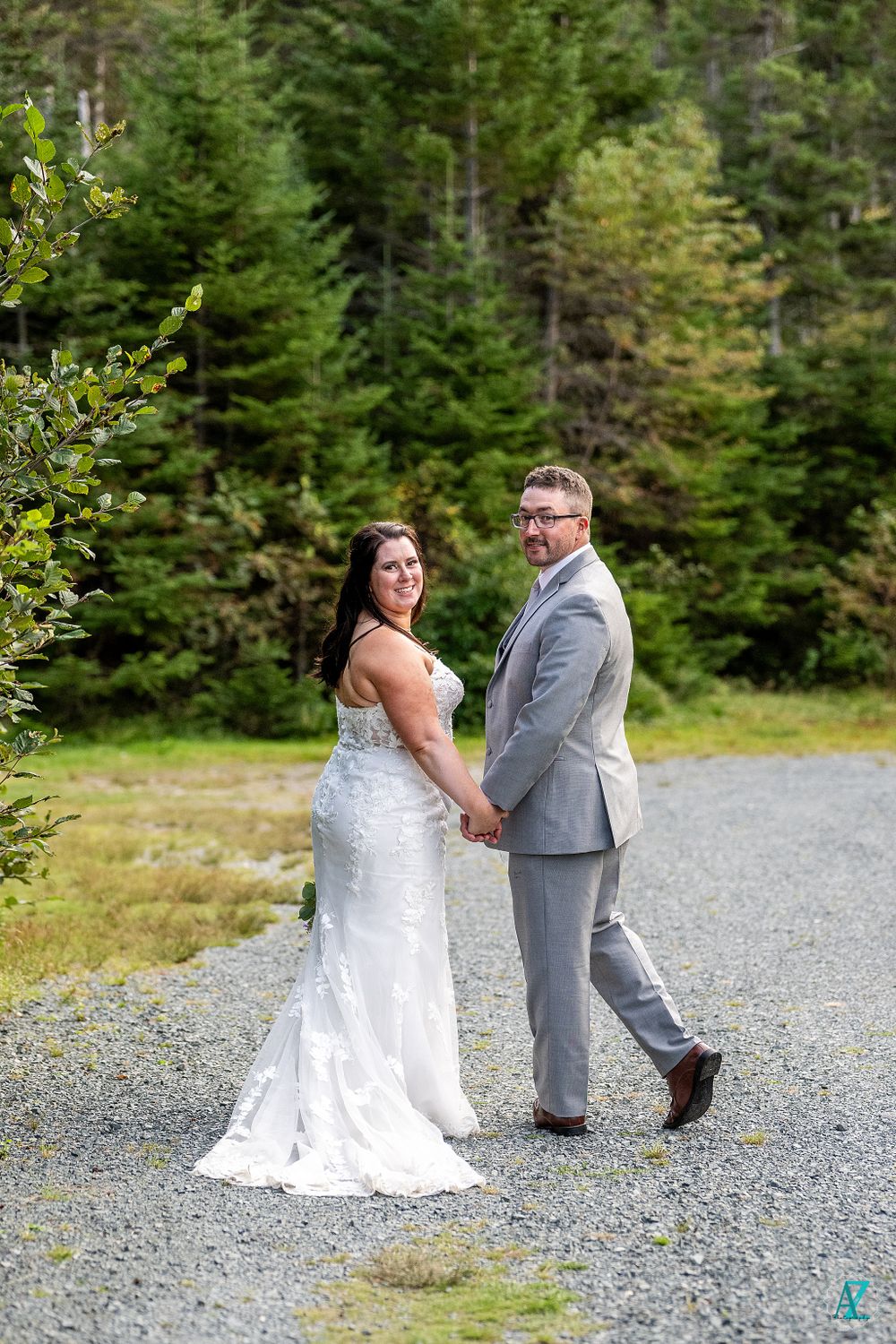 Romantic wedding portrait on a forest path with evergreen trees in background.