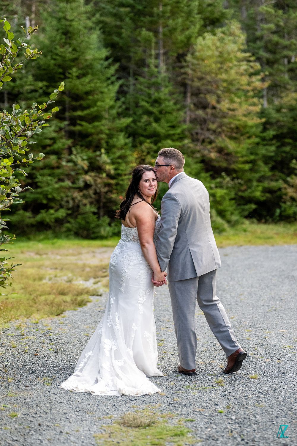 Wedding couple shares a playful moment on gravel path surrounded by pine forest.