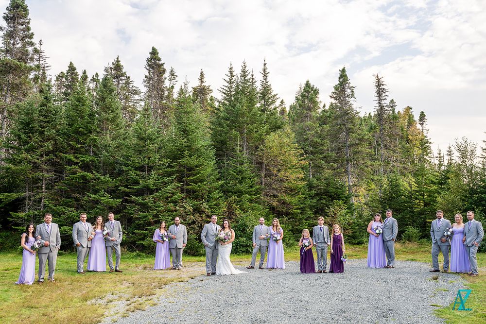 Wedding party in purple and grey attire lined up on forest path for group photo.
