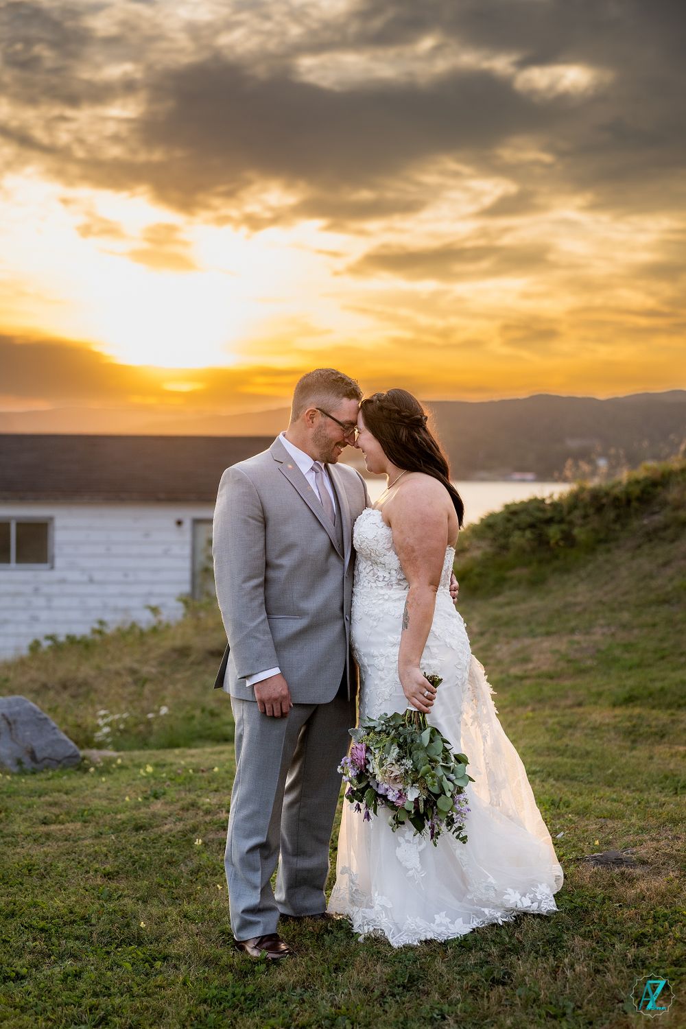 Newlyweds share intimate moment at sunset with mountainous landscape in background.