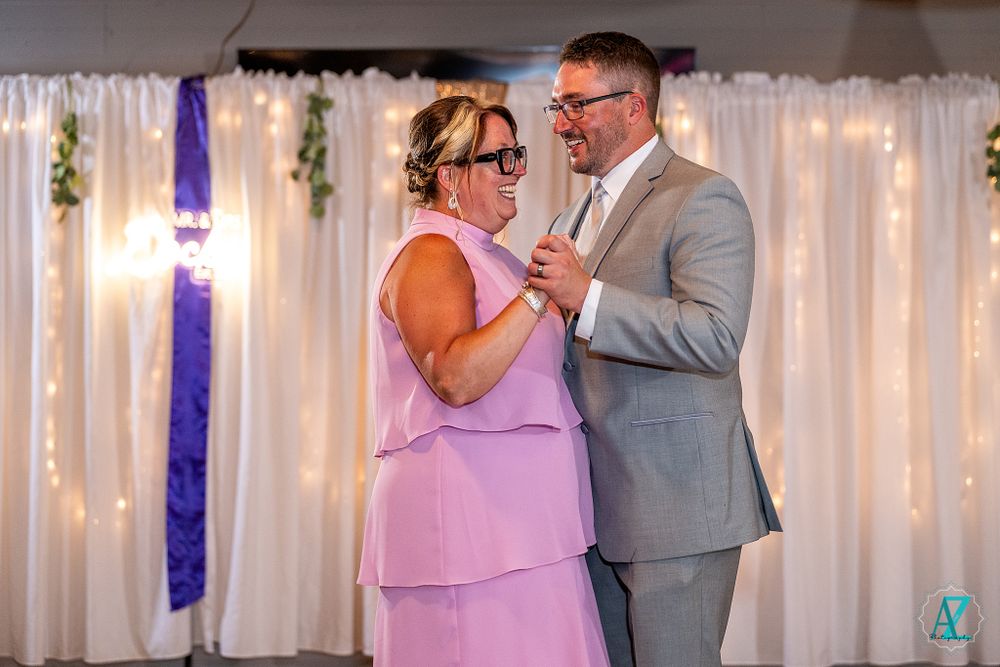 A tender moment during a wedding dance between two people in formal attire with twinkle lights behind.