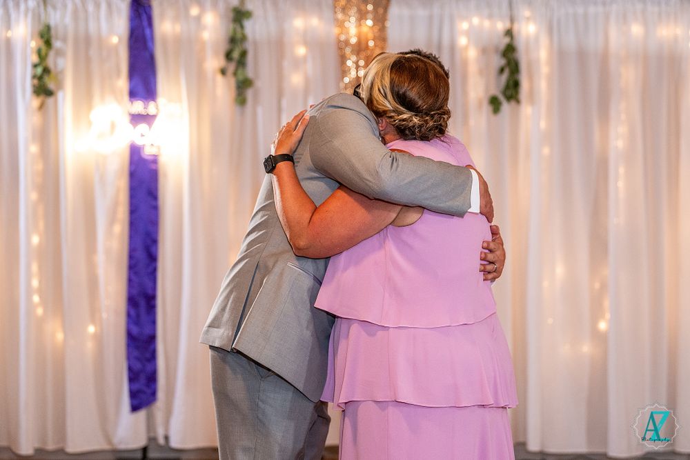 Emotional embrace during wedding dance with white backdrop and string lights.