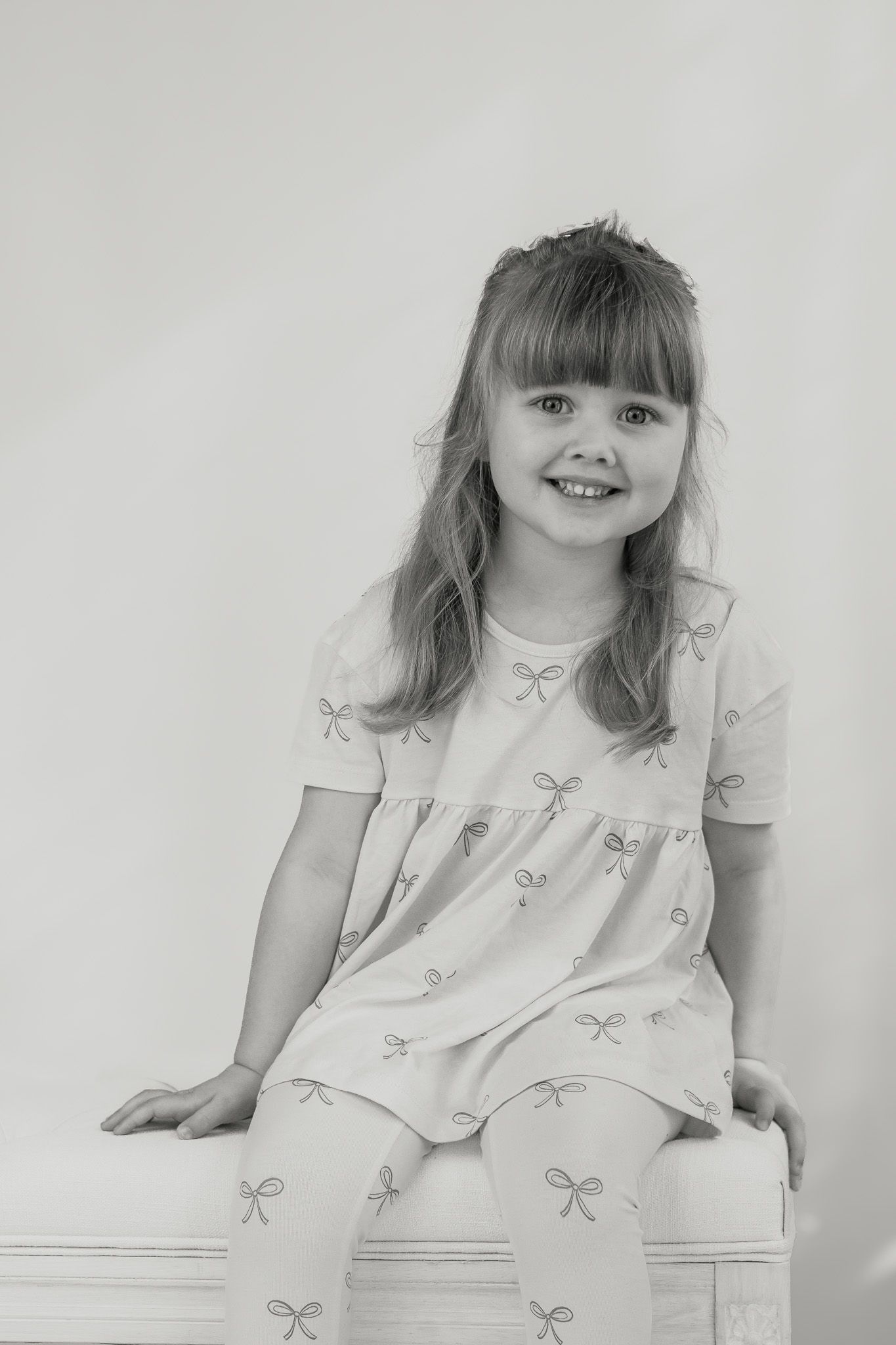 Black and white portrait sitting on white furniture in a bow-patterned dress.
