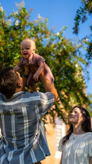 Parents playing with baby outdoors on sunny day with joyful expressions.