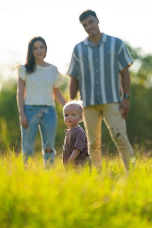 Family walking through tall grass field during golden hour sunset.