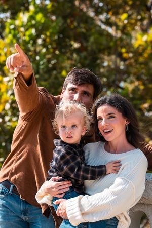 Happy family with young toddler outdoors in autumn park, father pointing at something in distance.