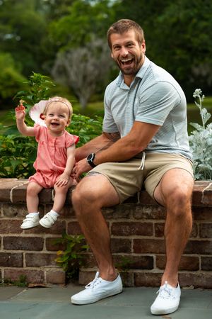 Parent and child share joyful moments while sitting on brick wall outdoors.