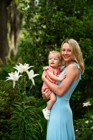 Mother and child share tender moment near blooming white lilies in garden.