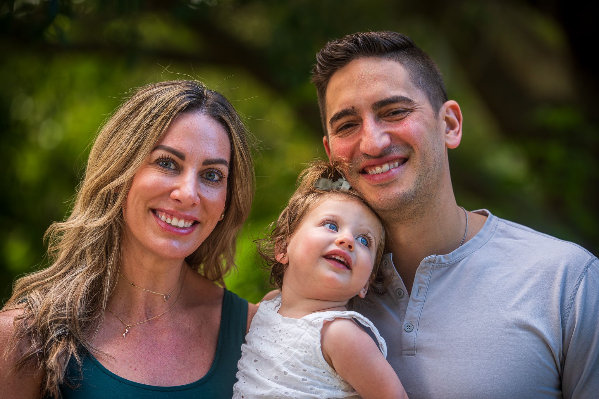 Family posing together outdoors with trees and natural lighting in the background.