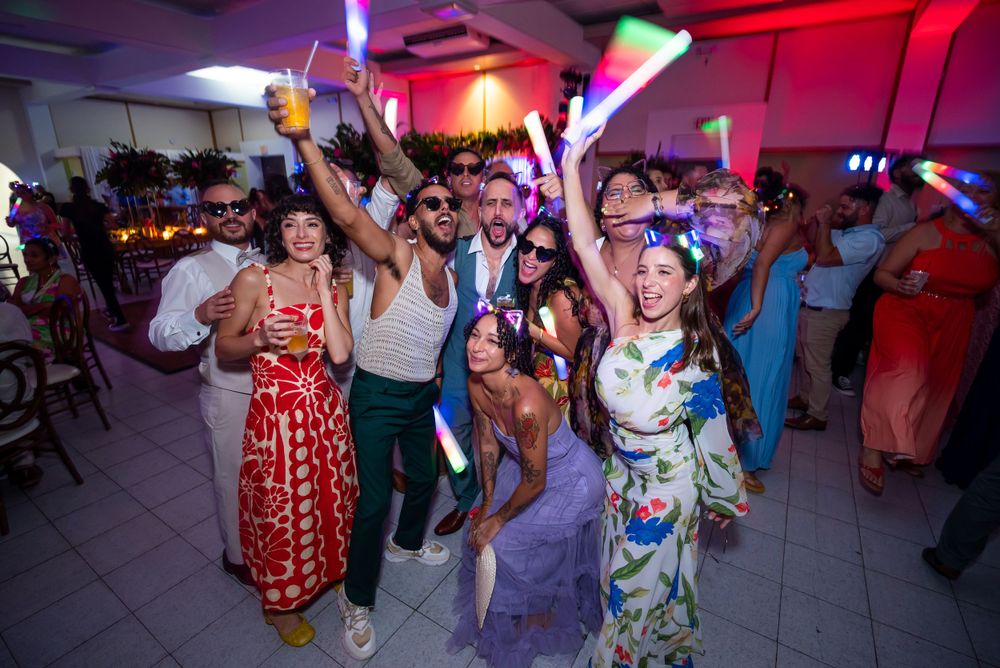 Festive party scene with people dancing and celebrating under colorful lighting at an indoor venue.