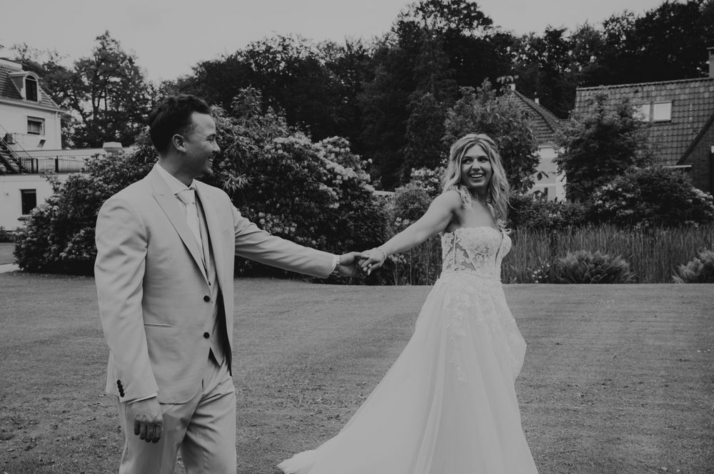 A couple shares a joyful candid moment on their wedding day in a black and white photograph on an outdoor lawn.