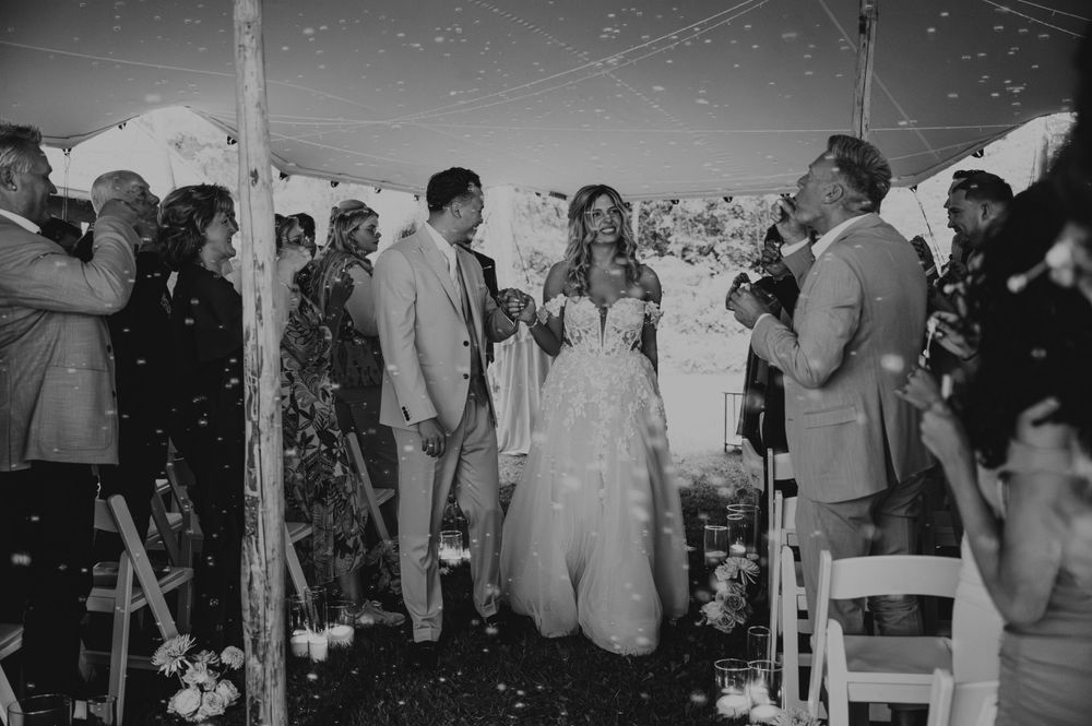 A black and white photo of wedding guests celebrating with confetti during an outdoor ceremony.
