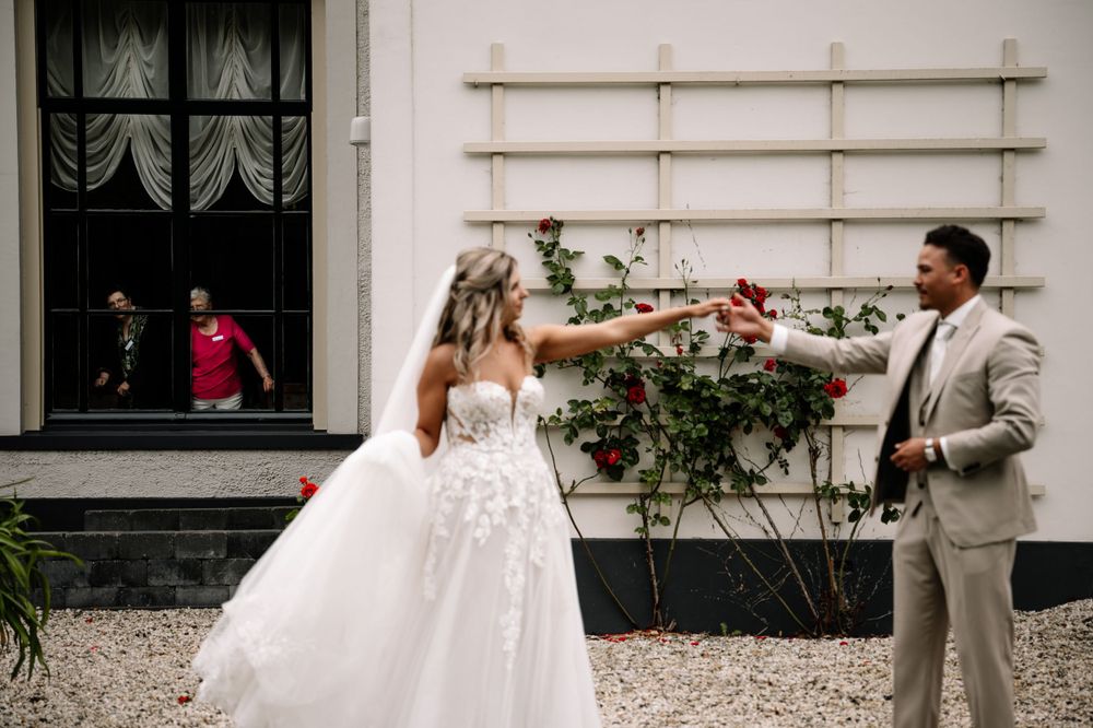 Playful wedding couple interacting outside a white building with lattice decor.