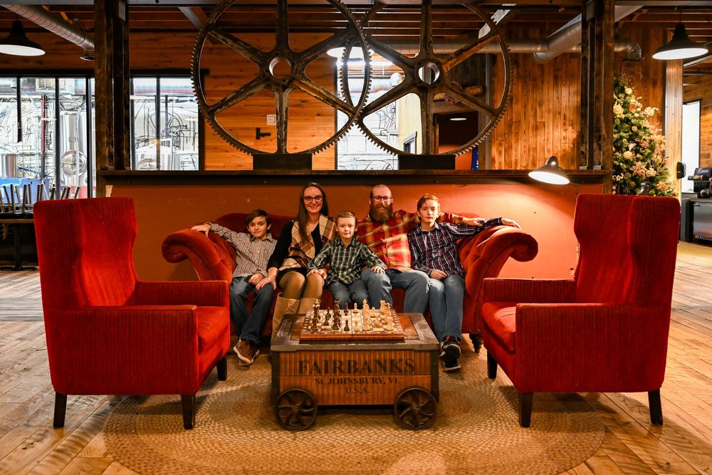 Family of five smiling together on red velvet sofas around a Fairbanks coffee table in a cozy lodge-style interior.