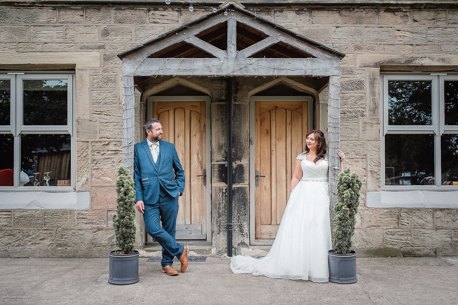 Wedding portrait of couple standing by rustic wooden doors of stone building.