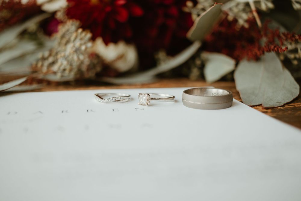 Close-up of wedding rings and diamond engagement ring resting on a white wedding invitation with floral decor.