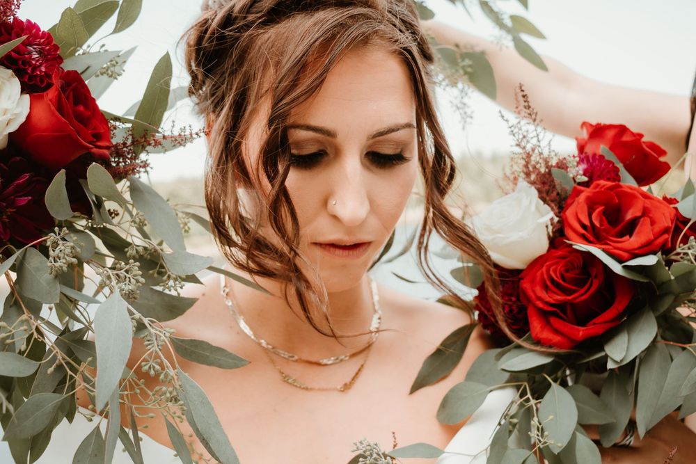 Close-up of a bride surrounded by lush greenery and red and white roses in her wedding bouquet.