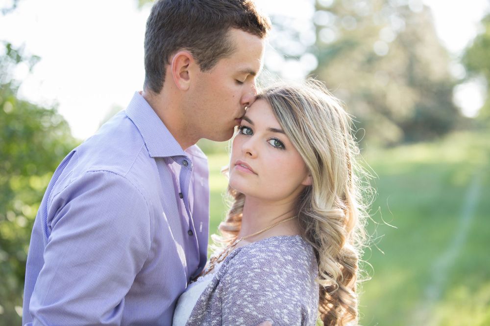 Couple shares loving glances during engagement photoshoot in natural setting.