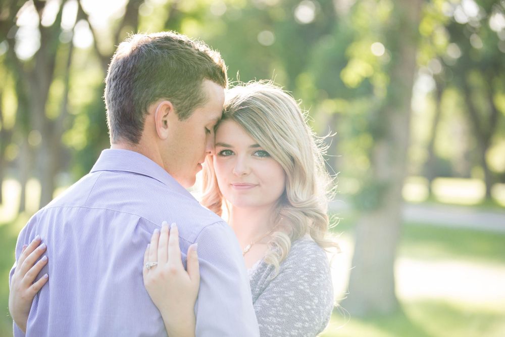 Couple embraces in a romantic outdoor photoshoot with natural lighting and trees.