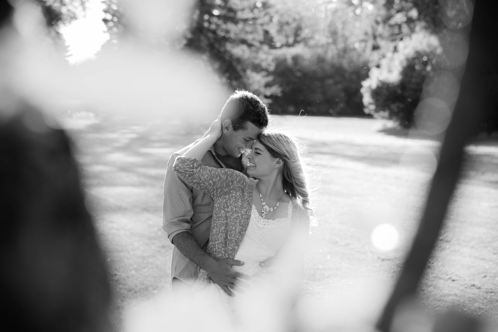 An artistic black and white capture of a couple's intimate moment through tree branches.